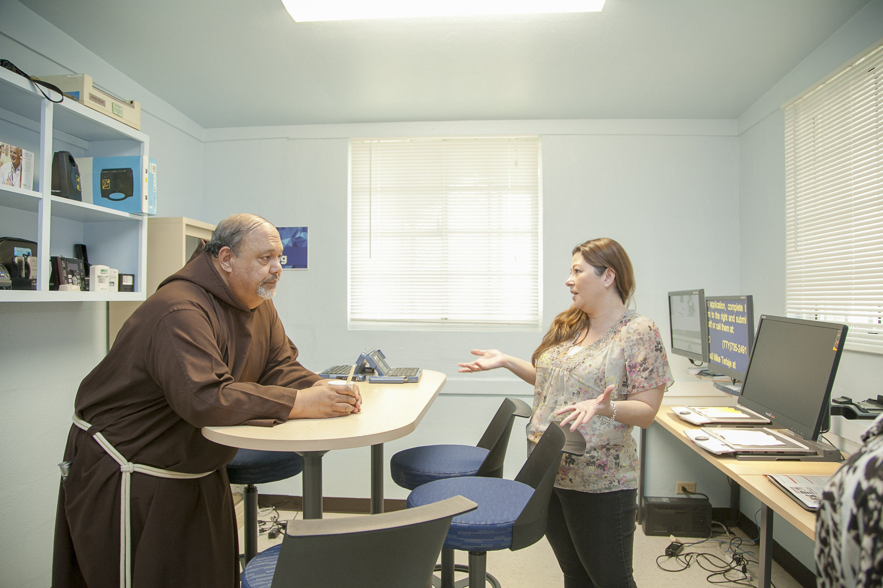 (Left to right) Father Joe listens while Carla Torres shares information on the various AT devices available for people with visual impairments. 