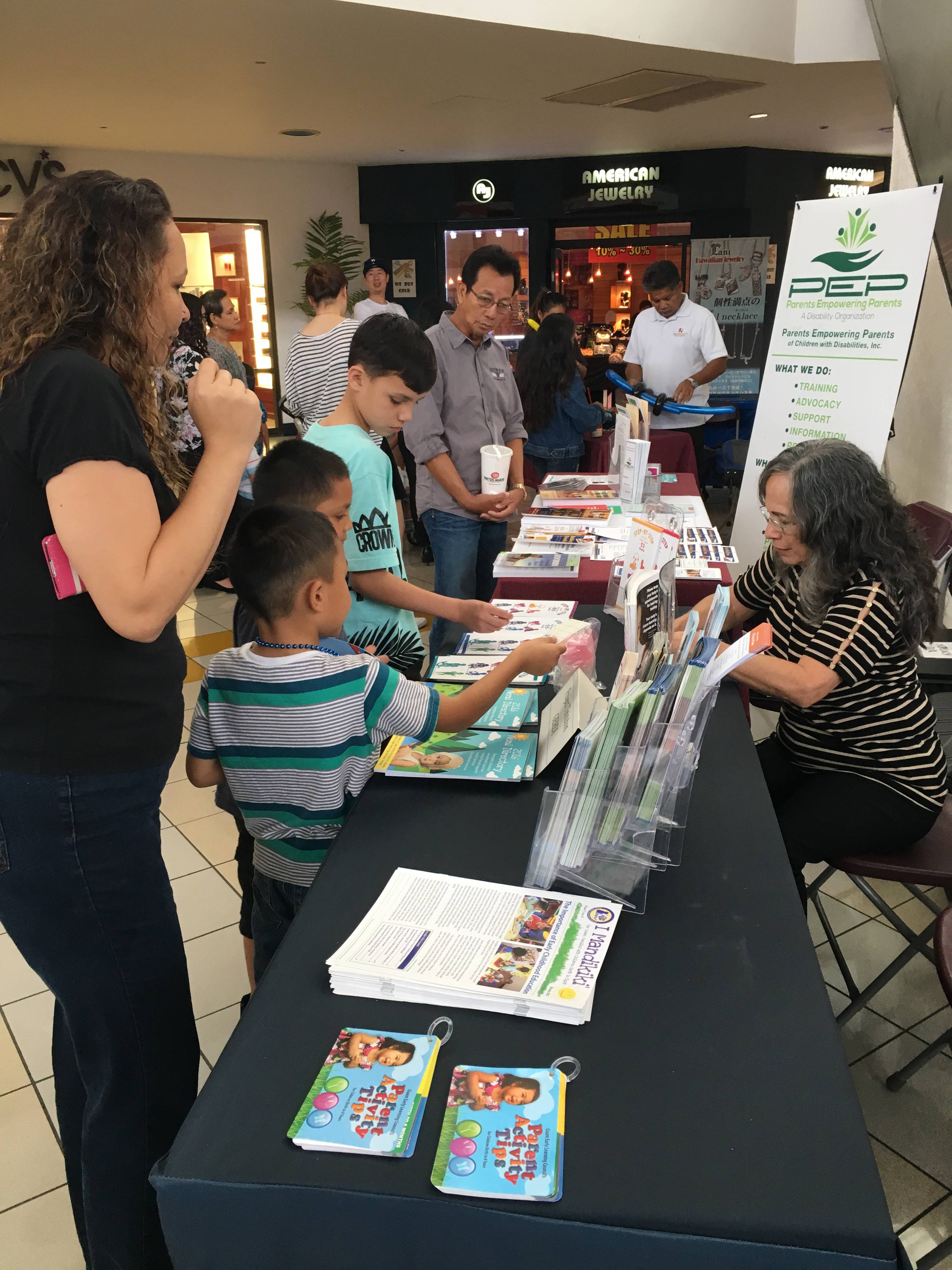 Dawn Guerrero (seated at right), Guam CEDDERS Grant Assistant, responds to questions from participants at the Dental Fair held on Sunday, February 28, 2016 at the Micronesia Mall.  On display and for dissemination were a variety of Guam CEDDERS products including Parent Activity Tip Cards, I Mandikiki' Newsletter, the 2016 Neni Directory of Services, and several brochures on the Guam Early Hearing Detection and Intervention (Guam EHDI) program and information that promotes the importance of Early Childhood Development and developmental screening.