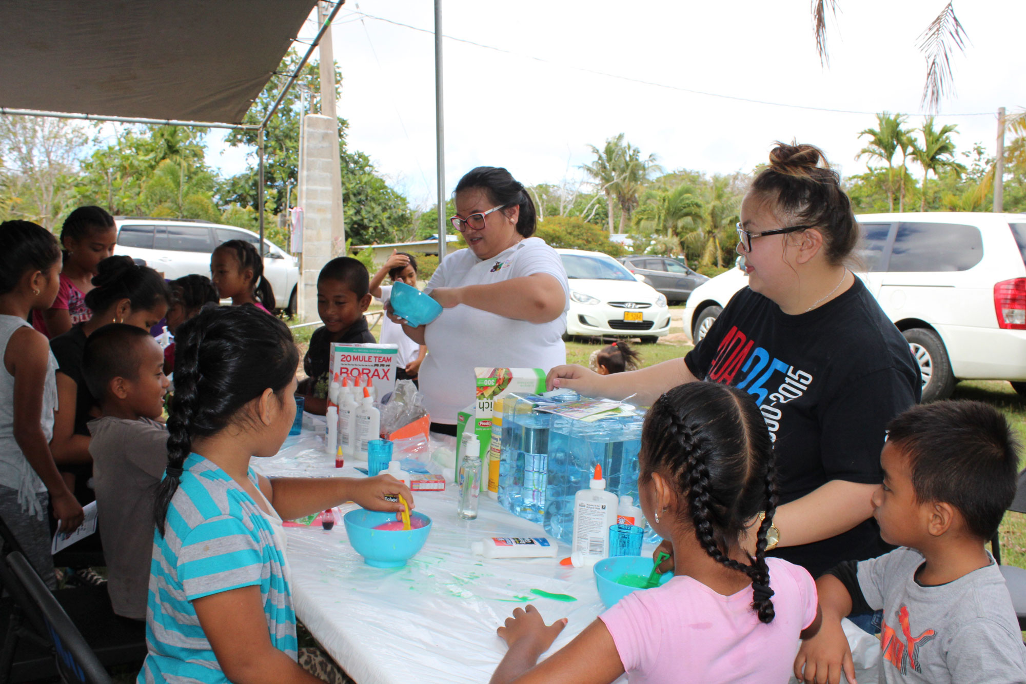 Terry Naputi, Guam CEDDERS Research Associate (back, left), and Jenika Ballesta, Research Associate (standing, right), assist children in making GAK out of simple household products at Gill Baza, Yigo on June 16.